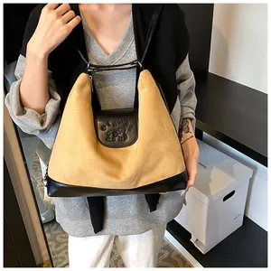 Detail of camel suede tote bag featuring a black leather logo flap and dual shoulder straps