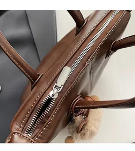Close-up of smooth silver metal zipper and white stitching on brown leather tote bag