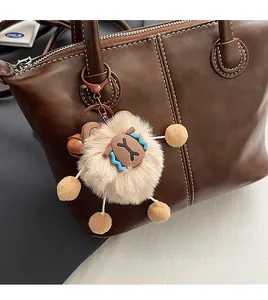 Close-up of a cute beige plush animal charm with a metal carabiner on a brown handbag