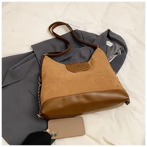 Close-up of brown suede and smooth leather texture with metallic chain on large shoulder bag