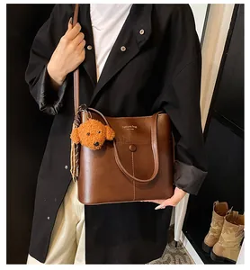 Detailaufnahme braune Leder-Eimertasche mit Plüschwelpen-Anhänger und New York Schriftzug
