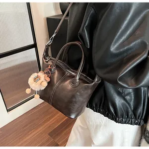 Close-up of retro brown leather tote with white stitching detail and plush charm