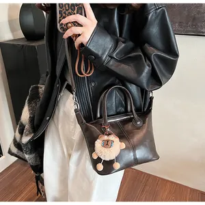 Detail of dark brown glossy leather tote bag featuring a cute plush lion charm accessory