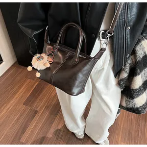 Deep coffee leather tote bag with round handles and plush pendant on model detail