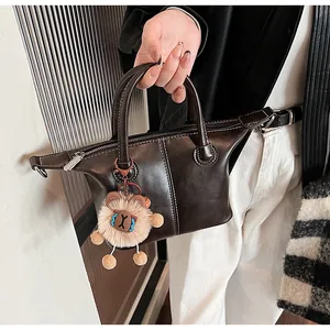 Detail of dark brown leather tote with contrast white stitching and plush charm