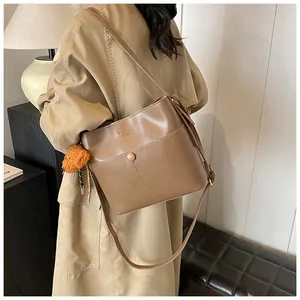 Detailansicht einer braunen Eimer-Tasche aus Leder mit dekorativem Plüsch-Anhänger