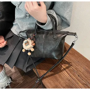 Detail of vintage black leather tote featuring contrast stitching and plush mascot charm