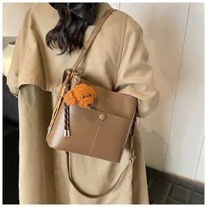 Detail der dunkelkhaki Beuteltasche mit Plüschhund-Anhänger und verstellbarem Riemen am Trenchcoat
