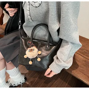 Detail of black leather tote bag with plush charm and adjustable shoulder strap worn by model