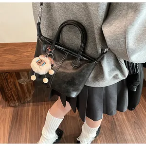 Detail of black faux leather tote bag with white stitching and lion plush charm decoration
