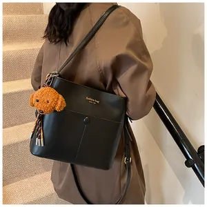 Detail einer schwarzen Beuteltasche mit Plüschanhänger und goldenem Modeschriftzug