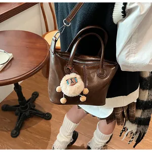 Detail of a dark brown leather Boston bag with white stitching and a plush sheep charm
