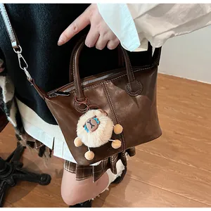 Detail of dark brown leather tote bag with zip closure and white sheep charm accessory