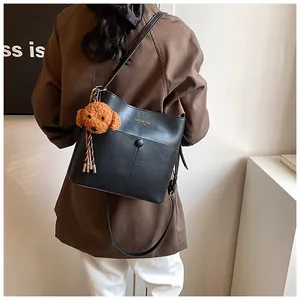 Detail der schwarzen Leder-Beuteltasche mit Metalldruckknopf und Plüschhund-Anhänger