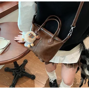 Detail of a dark brown leather tote bag with white contrast stitching and lion pendant