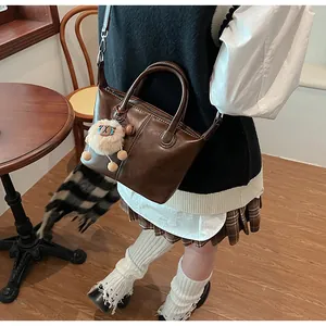 Detail of dark brown leather tote bag with round handles and white plush sheep pendant