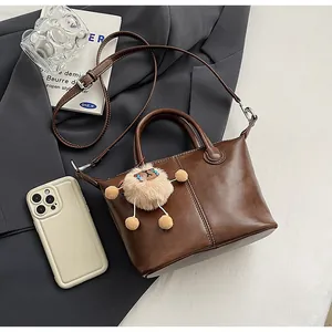 Detail of a dark brown leather tote bag with stitch decor, silver hardware and plush charm