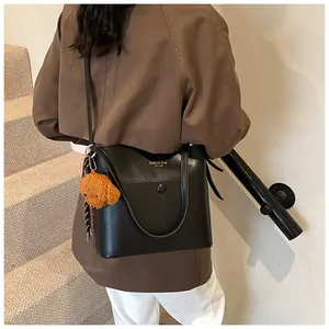 Detailansicht einer schwarzen Leder-Eimertasche mit Bärenanhänger und Seidenschal-Dekoration