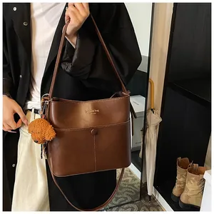 Detail einer dunkelbraunen Leder-Eimertasche mit Goldbuchstaben und Bärenanhänger