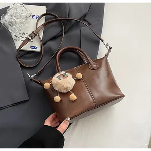 Detail of dark brown leather tote with white stitching and plush sheep charm