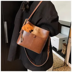Detail der braunen Vintage Beuteltasche mit Hundeplüsch-Anhänger und Modeschriftzug