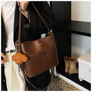 Detailaufnahme der braunen Leder-Eimertasche mit Goldaufdruck und Plüsch-Anhänger