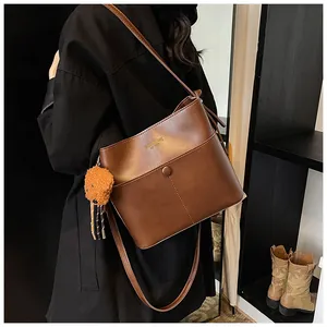 Detailansicht der dunkelbraunen Leder-Beuteltasche mit Plüschbär-Anhänger und Goldtext