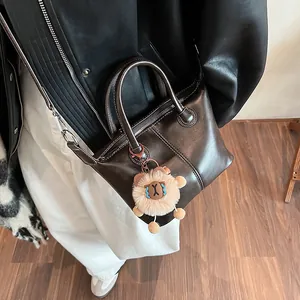 Minimalist dark brown leather tote bag with plush lion pendant and thin shoulder strap