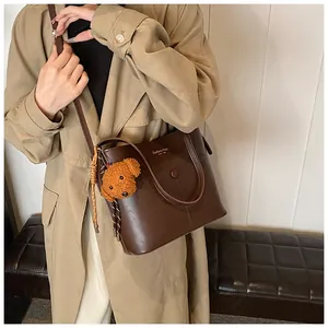 Modische Eimer-Tasche aus dunkelbraunem Leder getragen mit Trenchcoat und Plüsch-Anhänger