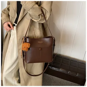Detailaufnahme der braunen Beuteltasche mit Plüschbär-Anhänger und Zierschleife aus Leder
