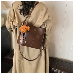 Detail der braunen Leder-Eimertasche mit Modetext und orangefarbenem Plüschtier-Anhänger