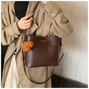 Braune Beuteltasche mit Plüschbär-Anhänger, getragen von Model im schicken Trenchcoat