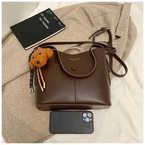 Detailansicht der dunkelbraunen Beuteltasche mit Plüsch-Anhänger und Smartphone