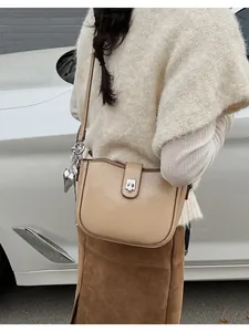 Detail of beige saddle bag with lychee texture, metal buckle and heart charm