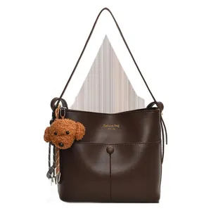 Minimalistische dunkelbraune Beuteltasche mit Goldaufschrift und braunem Plüsch-Anhänger