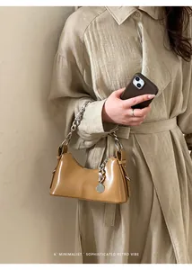 Dettaglio borsa a mezzaluna in pelle color caramello con catena d'argento e ciondolo