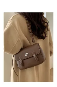 Detail of a dark brown pebble grain leather crossbody bag worn with a camel coat