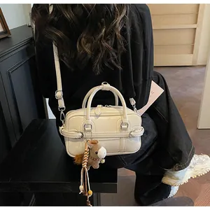 Detail of a creamy white Boston handbag with a brown horse plush charm shown on a model