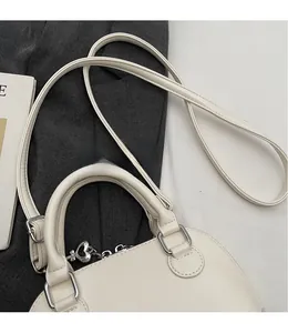 Detail of beige shell bag featuring smooth leather texture and silver metal strap rings