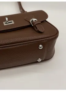 Detail of silver buckles and protective rivets on brown lychee grain leather bag