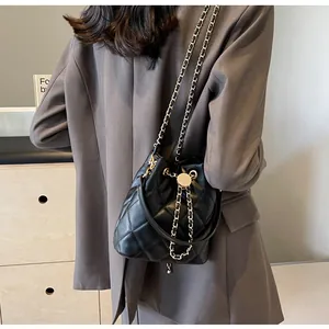 Detail of black quilted leather bucket bag with gold chain strap on a blazer outfit
