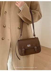 Minimalist brown pebbled leather satchel bag styled with a beige coat in an indoor setting