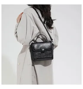 Detail of a black shimmering crossbody bag with a handle worn over a trench coat