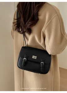 Minimalist black pebble leather messenger bag with silver twist lock on a camel coat
