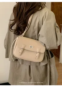 Detail of beige square messenger bag with pebble texture and metallic twist lock on coat