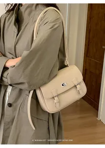 Detail of beige lychee leather crossbody bag with silver twist lock on green trench coat