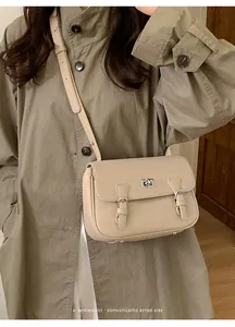 Detail of off-white lychee leather crossbody bag featuring metal clasp on khaki coat