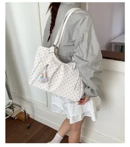 Detail of white polka dot tote bag featuring a star charm and bunny pendant accessory