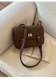 Detailed view of brown lychee leather bag with silver metal twist lock on a white sofa