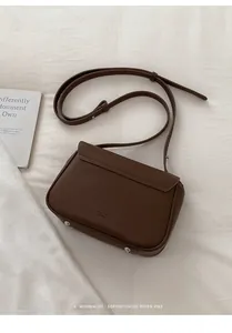 Detailed view of dark brown pebbled leather crossbody bag with flap and metal studs